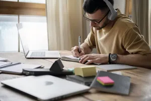 Ensino EAD na Estácio: jovem sentado de frente para mesa com notebook e cadernos abertos.