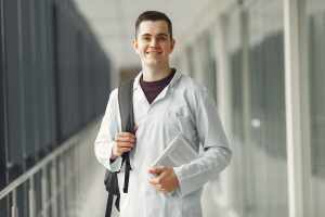 Estudante de medicina com jaleco branco e mochila nas costas parado em um corredor. Imagem ilustra como conseguir o FIES para Medicina em 2023.
