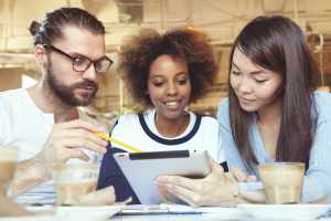 Quem pode ser fiador do Fies? Tres jovens estudantes olham juntos para a tela de um tablet.