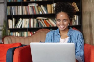 Jovem negra sentada com notebook no colo fazendo a inscrição para o Enem 2023.
